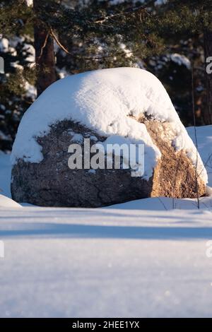 Helsinki / Finlandia - 10 GENNAIO 2022: Una scena rurale di sole giornata invernale con un blocco di granito coperto di neve. Foto Stock