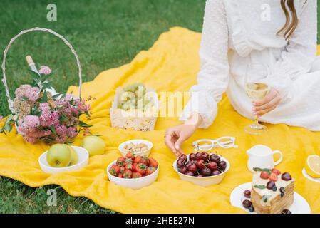 Picnic estivo in natura con torta, succo di frutta e frutta su una coperta gialla tra l'erba verde. Attività all'aperto Foto Stock
