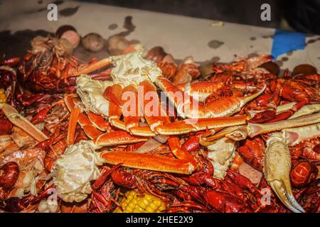 Artigli di granchio e gamberi e gamberi arroccati su un cavo coperto di carta con spighe di mais e cipolle ad un punto di ebollizione di pesce - poco profondo fuoco Foto Stock