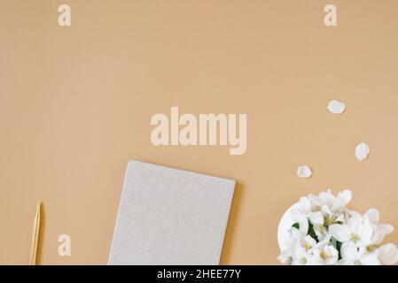 Lavoro da casa concetto appartamento adagiato su tavolo beige con blocco note, penna e vaso di fiori. Vista dall'alto. Spazio di copia Foto Stock