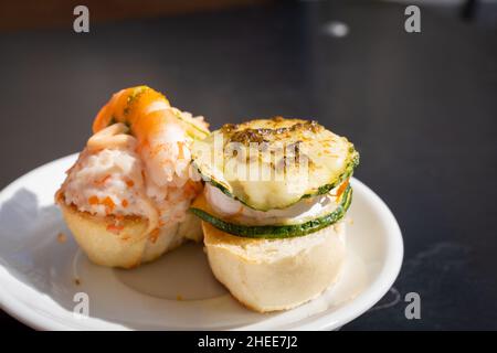 Deliziose tapas spagnole sul piatto con pane, gamberi, formaggio e zucchine in cima. Cibo da ristorante, snack da bar, concetti gourmet Foto Stock