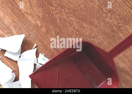 shards e paletta sul pavimento. Paletta e schegge di una piastra rotta. Vista dall'alto vista dall'alto. Il concetto di pulizia della casa, crisi e problemi. Foto Stock