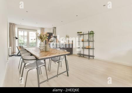 Tavolo da pranzo con fiori in vasi posti vicino al banco della cucina e decorazioni su ripiani in spazioso appartamento con porta di vetro Foto Stock