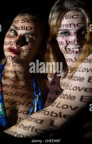Sorridenti femmine che guardano la telecamera al buio illuminata dal proiettore che proietta testo ombra che copre il volto Foto Stock