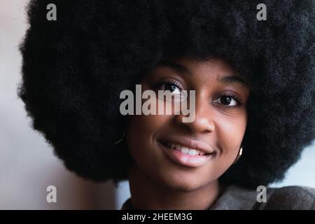 Ritratto di felice attraente afroamericana femmina con elegante acconciatura nero afroafroguardando la macchina fotografica con sorriso in stanza luminosa Foto Stock