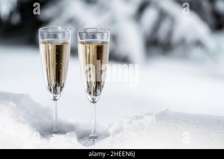 Primo piano di due flute di champagne che si rinfrescano nella neve sullo sfondo della natura invernale. Concetto di festa. Spazio di copia. Foto Stock