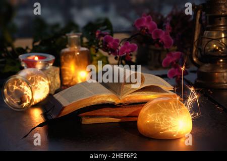 Luci magiche con scintille e bagliori arancioni in vari vasi di vetro. Inverno con luci e libri antichi. Pila di libri con uno aperto. Magenta, fucsia Foto Stock