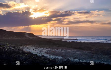 Tramonto vivace sul paesaggio di lava vulcanica sull'isola di Lanzarote in Spagna. Cielo drammatico con gli ultimi raggi del sole sul cielo nuvoloso sopra le isole Canarie. Onde di mare Foto Stock