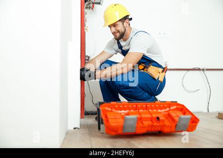 Tecnico di lavori duri, per l'idraulico in uniforme, utilizzare gli attrezzi della cassetta degli attrezzi durante l'installazione e il controllo dei tubi dell'acqua Foto Stock