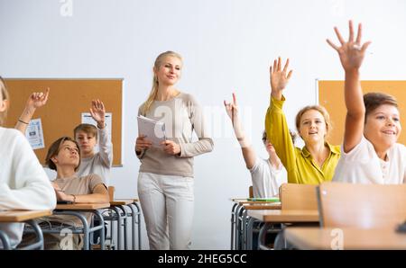 Gli allievi alzano le mani durante la lezione a scuola Foto Stock