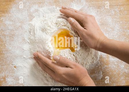 Panoramica delle mani di giovane donna su una pila di farina pronta per impastare pasta fatta in casa su tavola o tavola di legno Foto Stock