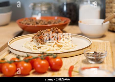Piatto con spaghetti bolliti servito con carne tritata fritta in piedi su tavola di legno con pomodori freschi e pepe Foto Stock