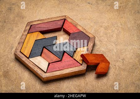 puzzle in tangram esagonale di legno contro carta corteccia testurizzata fatta a mano, teaser cervello e gioco divertente con diversi modi per risolvere Foto Stock