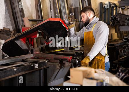 L'operatore taglia il tubo di profilo metallico su una sega a nastro Foto Stock