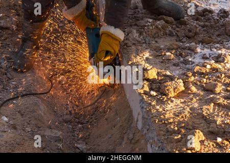 Un operaio taglia il metallo. Le mani di un operatore che taglia il metallo con una smerigliatrice elettrica. Processo di lavorazione in un cantiere. Taglio di metalli. Costruzione Foto Stock