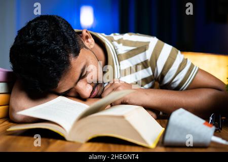 Giovane studente che dorme sul tavolo a causa della messa in onda della lettura per l'esame a casa - concetto di duro lavoro, pigrizia e tarda notte di studio Foto Stock