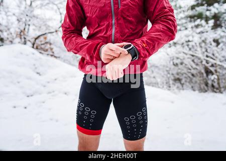 metà della sezione dell'uomo in piedi all'aperto nella giornata d'inverno controlla il suo orologio da polso intelligente per il tempo e la tariffa hart mentre si allenano atleta outdoor maschio runner utilizzando Foto Stock
