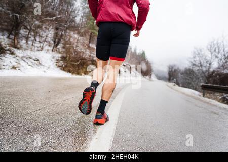 Un uomo caucasico adulto che corre in inverno atleta maschile allenamento runner su strada aperta in natura con neve intorno a salute e fitness concetto reale Foto Stock
