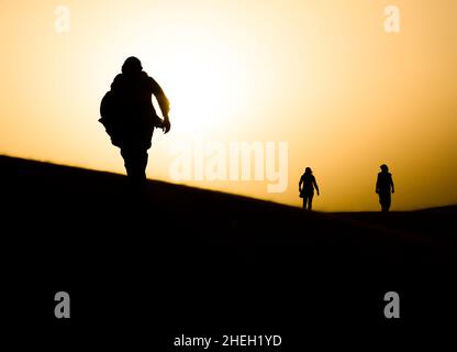 tre esseri umani vagano nel deserto del sahara durante il tramonto Foto Stock