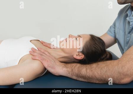 Paziente di sesso femminile in trattamento con collo e spalle osteopatici. Terapista che manipola la schiena della testa e del torace. Una ragazza che riceve il trattamento CST Foto Stock