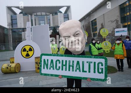 Berlino, Germania. 11th Jan 2022. Un attivista vestito come Cancelliere Scholz si trova di fronte ad una replica nucleare centrale presso la Cancelleria federale con un banner che recita 'sostenibile'. Sotto lo slogan "No al nucleare e al gas. Appello contro i piani di tassonomia della Commissione europea", un'alleanza di BUND, Campact, Deutsche Umwelthilfe e Greenpeace, tra gli altri, dimostra. Credit: Jörg Carstensen/dpa/Alamy Live News Foto Stock