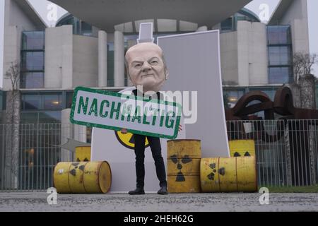 Berlino, Germania. 11th Jan 2022. Un attivista vestito come Cancelliere Scholz si trova di fronte ad una replica nucleare centrale presso la Cancelleria federale con un banner che recita 'sostenibile'. Sotto lo slogan "No al nucleare e al gas. Appello contro i piani di tassonomia della Commissione europea", un'alleanza di BUND, Campact, Deutsche Umwelthilfe e Greenpeace, tra gli altri, dimostra. Credit: Joerg Carstensen/dpa/Alamy Live News Foto Stock