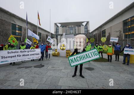 Berlino, Germania. 11th Jan 2022. Un attivista vestito come cancelliere Scholz si trova con una bandiera che legge 'sostenibile' con altri attivisti di fronte a una replica nucleare centrale presso la Cancelleria federale. Sotto lo slogan "No al nucleare e al gas. Appello contro i piani di tassonomia della Commissione europea", un'alleanza di BUND, Campact, Deutsche Umwelthilfe e Greenpeace, tra gli altri, dimostra. Credit: Jörg Carstensen/dpa/Alamy Live News Foto Stock