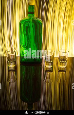 Una bottiglia verde con tre bicchieri da pallino sullo sfondo che si illumina con una pittura chiara. Foto Stock