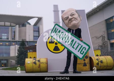 Berlino, Germania. 11th Jan 2022. Un attivista vestito come Cancelliere Scholz si trova di fronte ad una replica nucleare centrale presso la Cancelleria federale con un banner che recita 'sostenibile'. Sotto lo slogan "No al nucleare e al gas. Appello contro i piani di tassonomia della Commissione europea", un'alleanza di BUND, Campact, Deutsche Umwelthilfe e Greenpeace, tra gli altri, dimostra. Credit: Jörg Carstensen/dpa/Alamy Live News Foto Stock