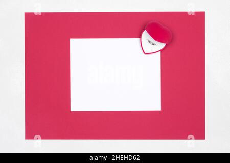 Carta bianca vuota con cornice rossa e scatola regalo a forma di cuore di velluto con anello per matrimoni all'interno. Spazio di copia Foto Stock