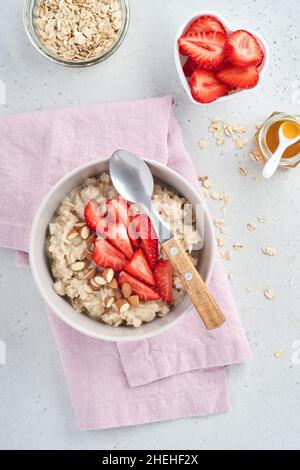 Porridge di farina d'avena con fette di fragola, mandorle noci e miele in ciotola per San Valentino sul tavolo grigio. Concetto per colazione o pasto romantico. Superiore Foto Stock