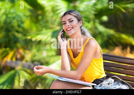 Ragazza studentessa adolescente all'aperto mantenendo una conversazione con il telefono cellulare Foto Stock