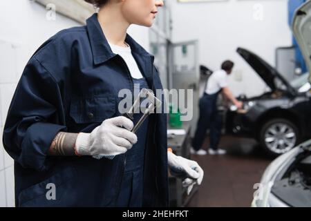 Vista ritagliata del meccanico in uniforme e dei guanti che tengono l'attrezzo in servizio auto Foto Stock