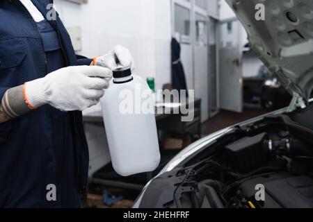 Vista ritagliata della donna da lavoro tatuata che tiene il barattolo nel servizio auto Foto Stock