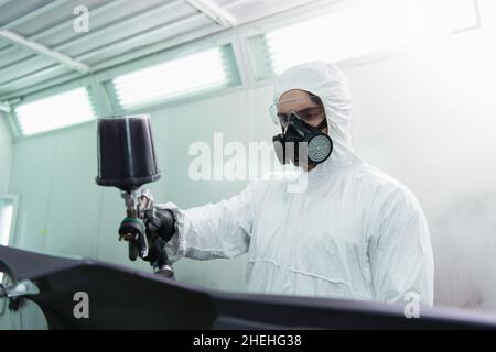 Uomo da lavoro in tuta e respiratore colorazione sfocata parte auto in servizio Foto Stock