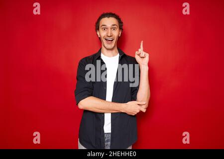 l'uomo eccitato punta indice dito su, si rallegra di una nuova idea brillante. isolato su sfondo rosso Foto Stock