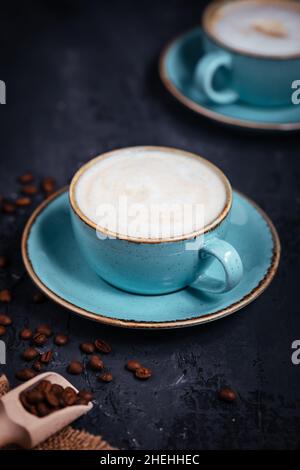 Caffè in tazze di porcellana blu su sfondo rustico di legno scuro con chicchi di caffè. Scena elegante e ordinata, caffe latte o macchiato espresso. Foto Stock