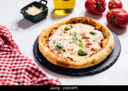 Pizza italiana tradizionale su sfondo bianco rustico con basilico, pomodoro, mozzarella, olio d'oliva e altri ingredienti. Foto Stock