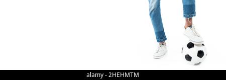vista ritagliata dell'uomo afro-americano in jeans e sneakers che giocano a calcio su bianco, banner Foto Stock