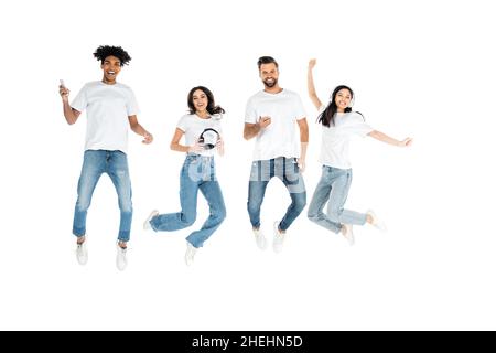 vista completa di amici multietnici con cuffie e telefoni cellulari che si levitating isolato su bianco Foto Stock