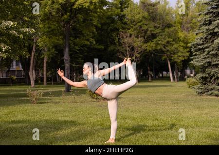 Giovane donna che pratica yoga nel parco pubblico all'alba Foto Stock
