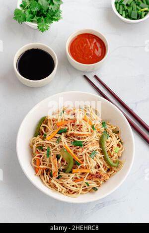Chicken Chow Mein semplice in una ciotola con scalogno, coriandolo e condimenti su sfondo bianco Top Down foto Foto Stock