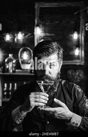 Barman hipster. Bell'uomo pensivo tiene un bicchiere di martini. Bell'uomo che beve alcool mentre si siede al bar. Foto Stock