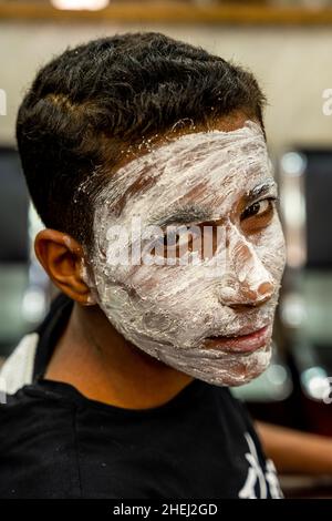 Un giovane uomo in Un salone di parrucchiere che indossa un Face Pack, Aqaba, Aqaba Governorate, Giordania. Foto Stock