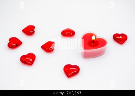 Una candela rossa nella forma di un cuore sta bruciando e i cuori di vetro sono distesi intorno. Concetto di amore, San Valentino, passione. Foto Stock