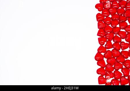 I cuori di vetro rosso brillante giacciono sulla destra su uno sfondo bianco. Concetto di amore, matrimonio, matrimonio, San Valentino, passione. Sfondo rosso festivo. Foto Stock