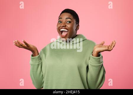 Eccitata femmina africana urla tenendo le mani vicino al viso, sfondo rosa Foto Stock