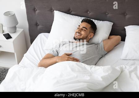 Ritratto di felice bel Guy Medio Oriente rilassarsi a letto a casa Foto Stock