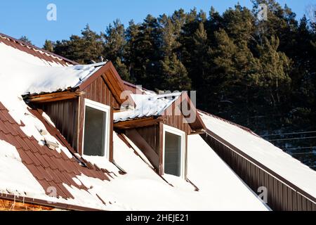 primo piano di una finestra di plastica mansarda su una casa di campagna, il tetto è coperto di neve Foto Stock