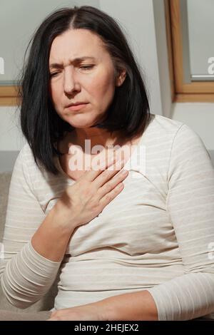 Donna matura di mezza età che ha un attacco di cuore. Donna che soffre di dolore toracico. Assistenza sanitaria e concetto cardiologico. Foto Stock